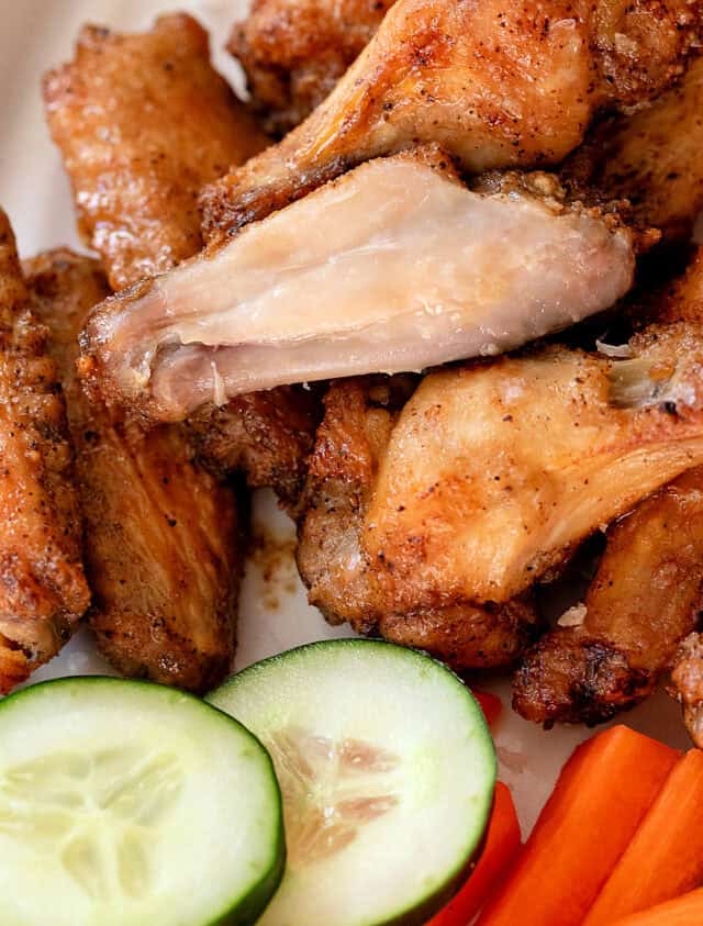 Closeup of salt and vinegar chicken wings, one without the skin to show how juicy the meat is. Cucumbers and carrots at bottom of picture.