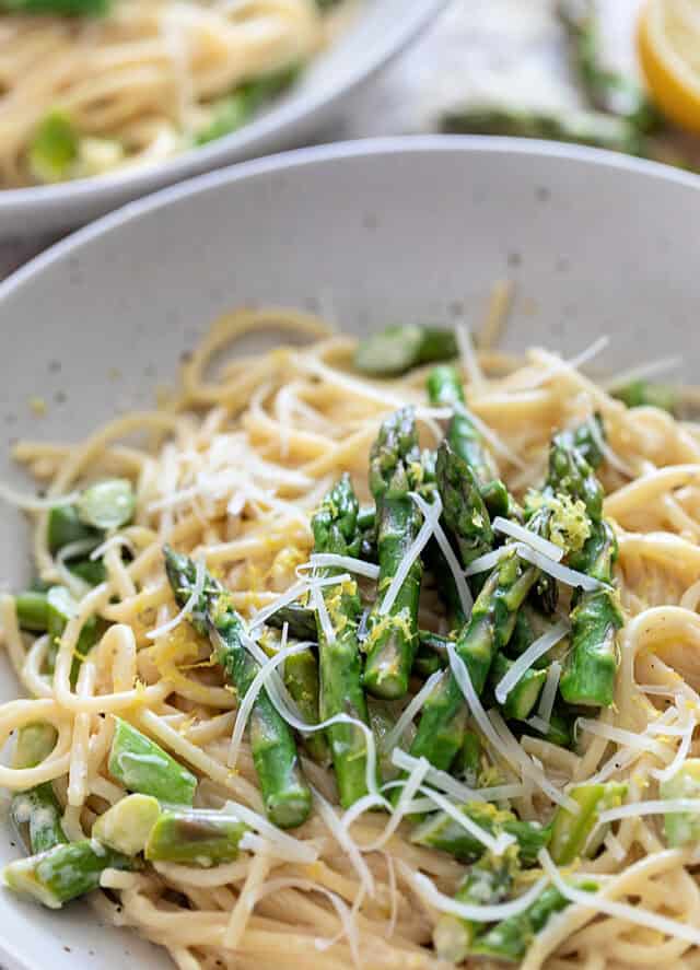 Closeup of Creamy Asparagus Pasta in white bowl with extra asparagus on top