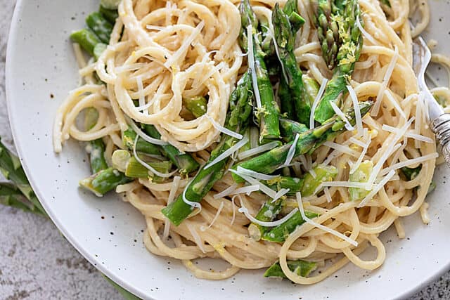 Closeup of pasta with cream sauce, asparagus and shredded parmesan and lemon zest.
