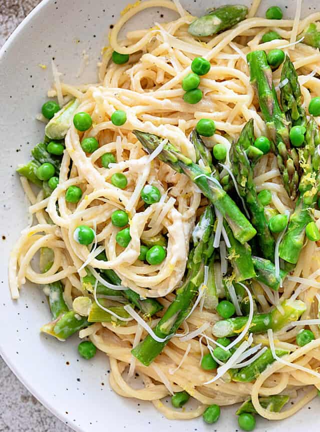 Creamy Asparagus Pasta in white bowl with extra asparagus and fresh peas on top
