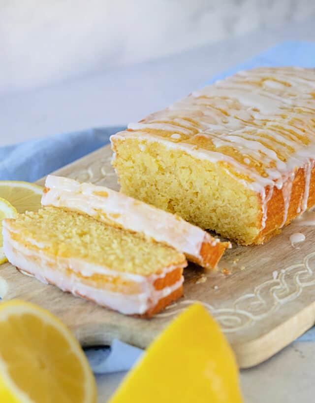 Lemon loaf on a cutting board, sliced with lemons in front.