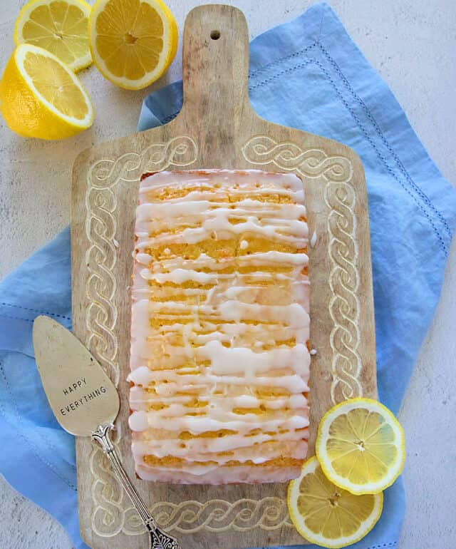 Moist lemon loaf on wooden serving tray with lemons.