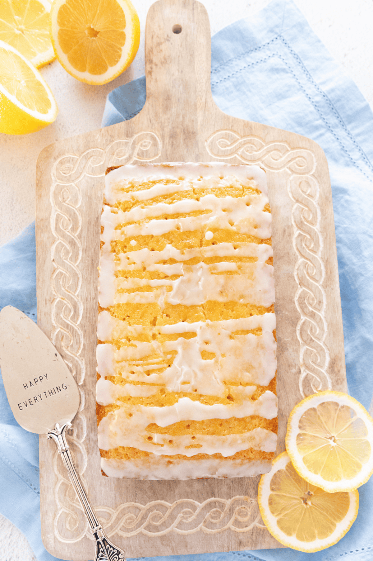 Lemon loaf on a wooden cutting board, glazed, with lemon slices.