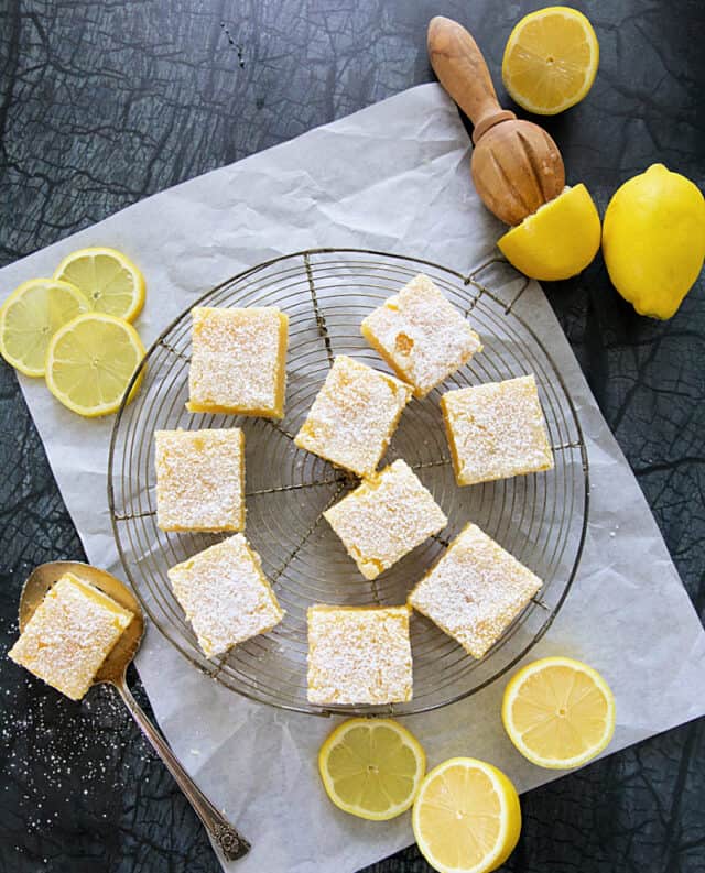 Lemon bars on a cooling rack with lemon slices all around.
