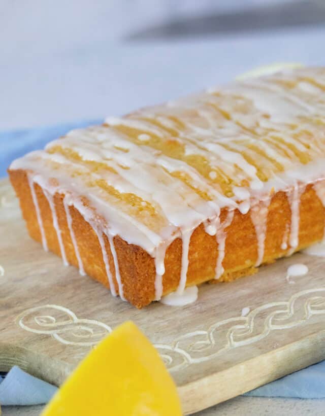 Moist lemon loaf with lemon glaze on wood platter.