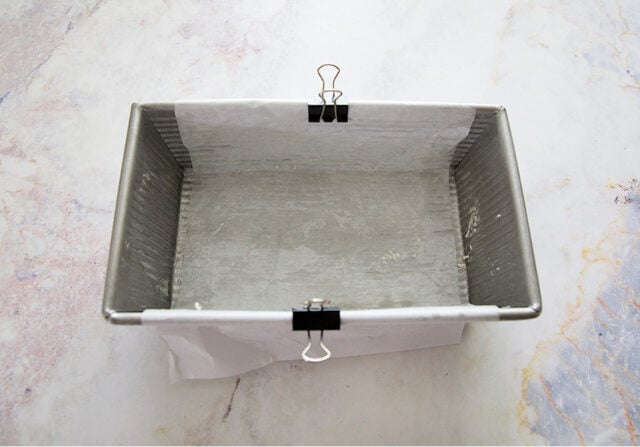 Loaf pan with parchment clipped on top to prevent from folding into lemon loaf as it bakes.