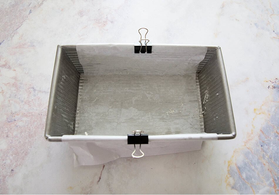 Loaf pan with parchment clipped on top to prevent from folding into lemon loaf as it bakes.