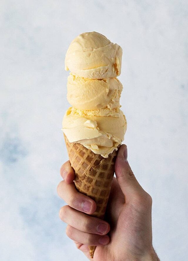 Pineapple ice cream in cone held in hand.