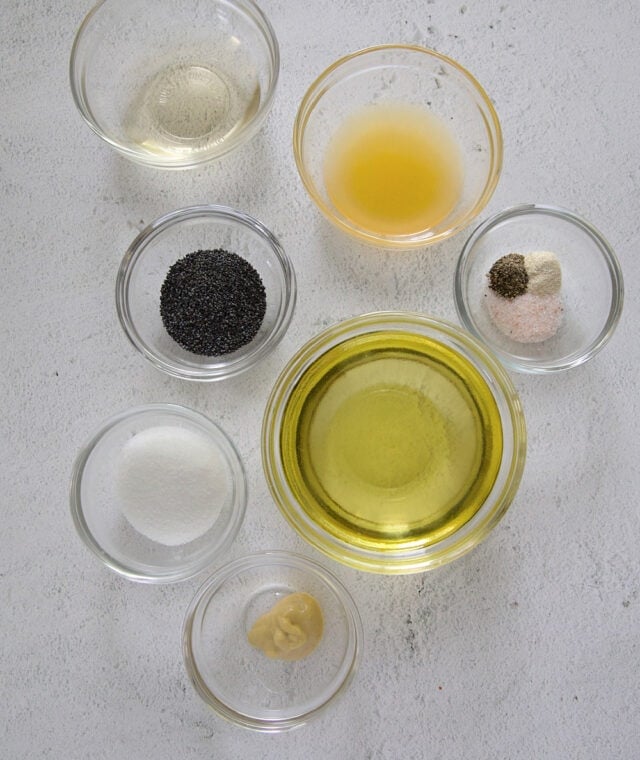 Ingredients in homemade poppy seed salad dressing. Top left going clockwise- White wine vinegar, orange juice, salt, pepper, and onion powder, olive oil mixed with other neutral oil, Dijon mustard, sugar, poppy seeds.