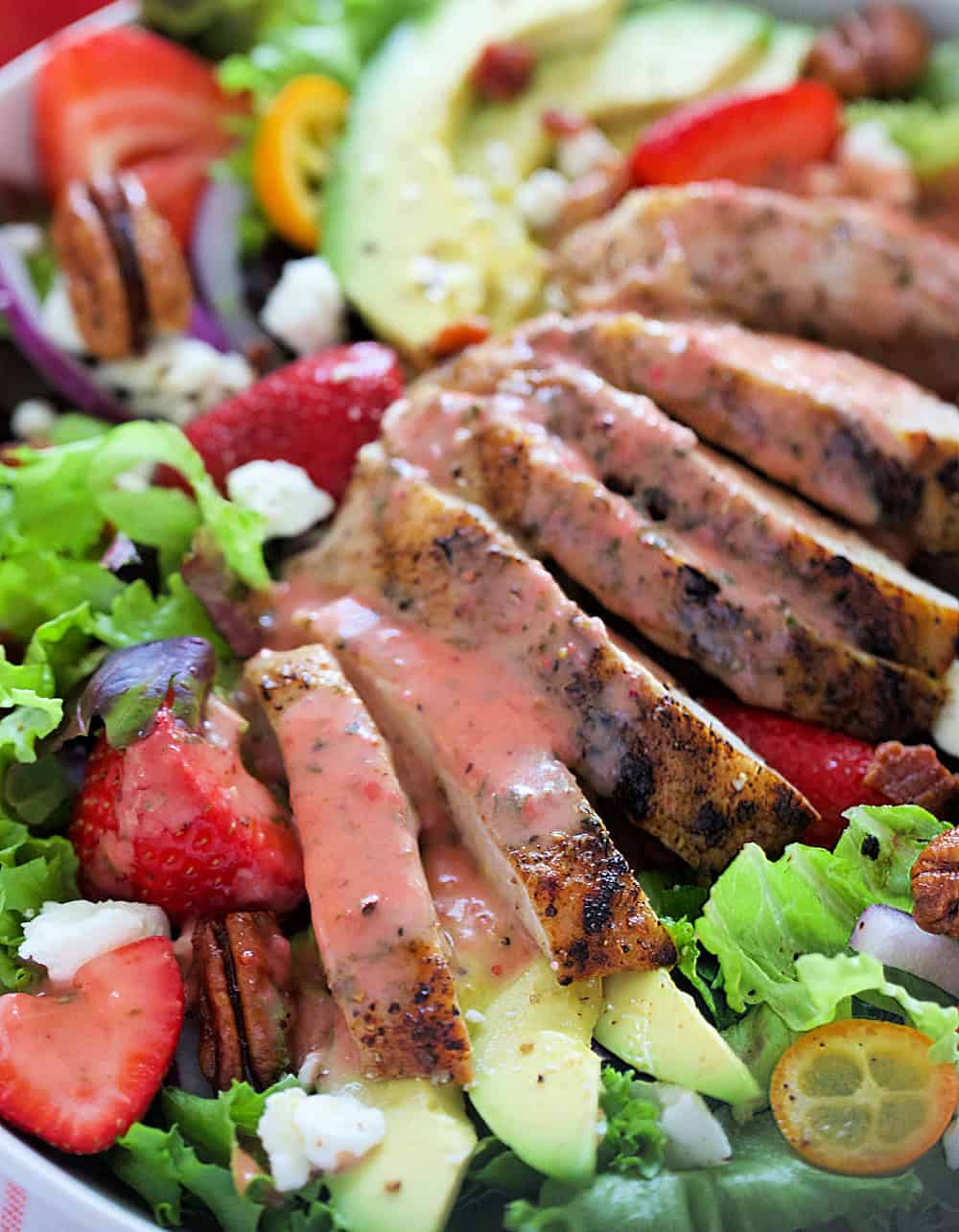 Closeup of grilled chicken with strawberry basil vinaigrette over strawberries and greens.