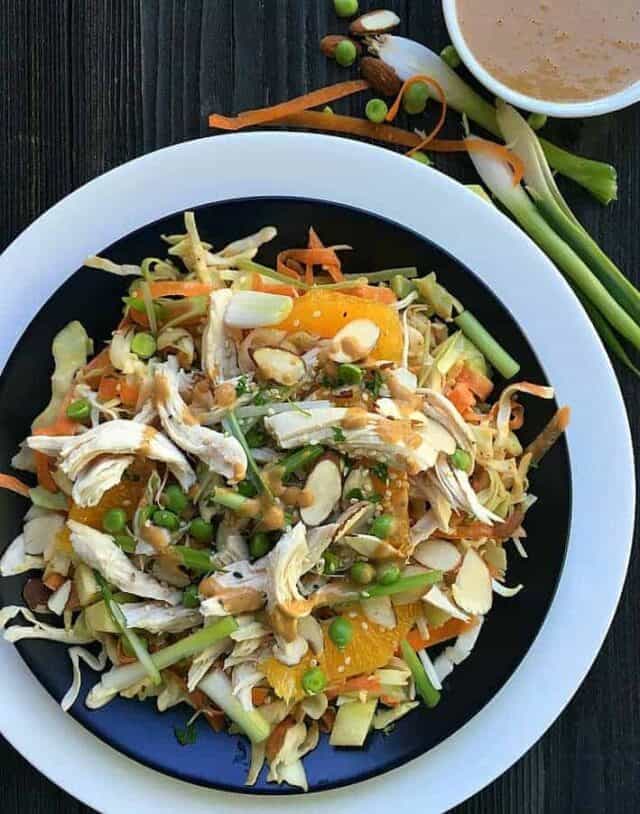 Chinese chicken salad on black and white plate with peanut sauce above.