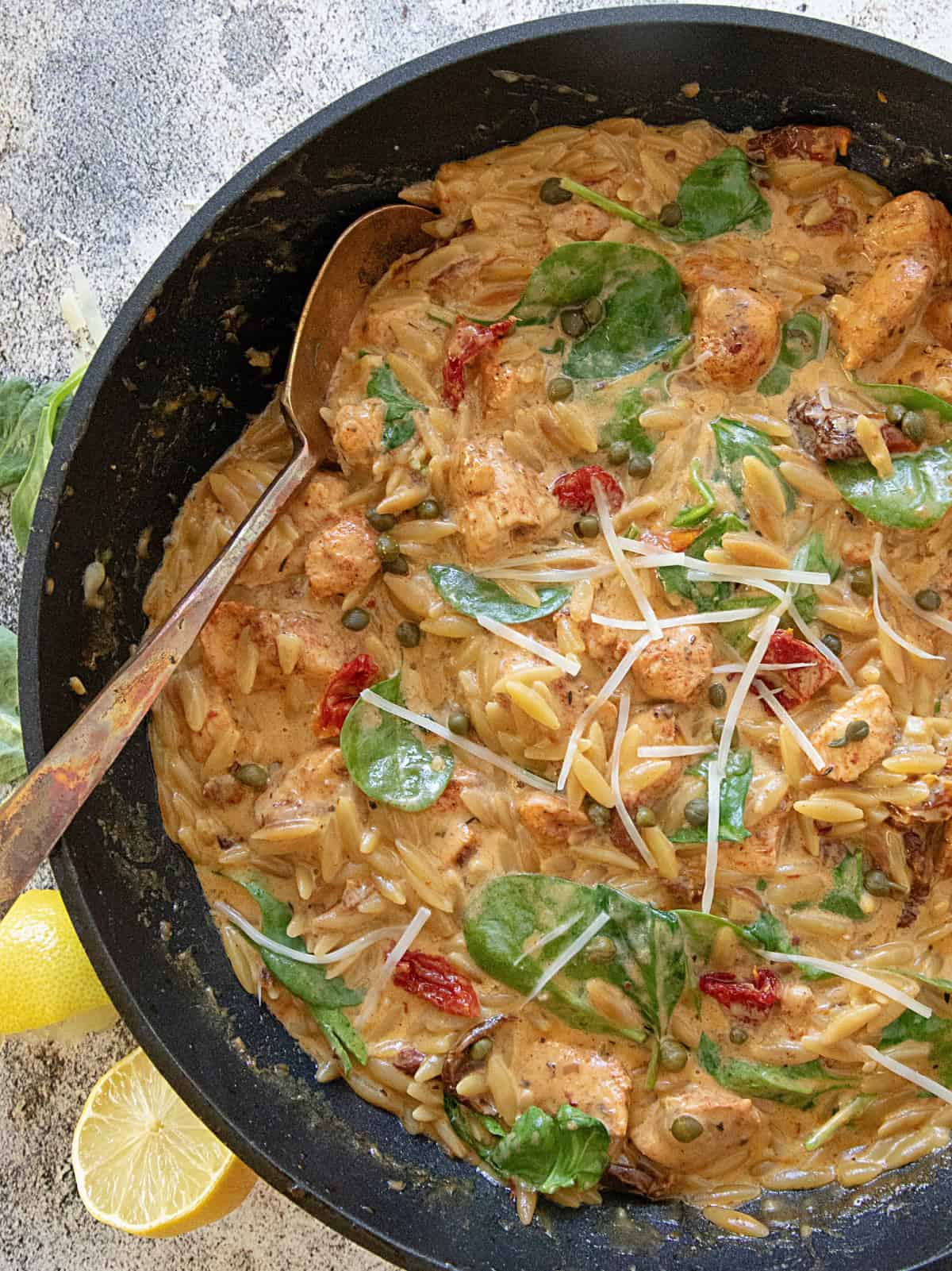 One Pot Creamy Chicken Orzo in the skillet it was cooked in. Lemons below.