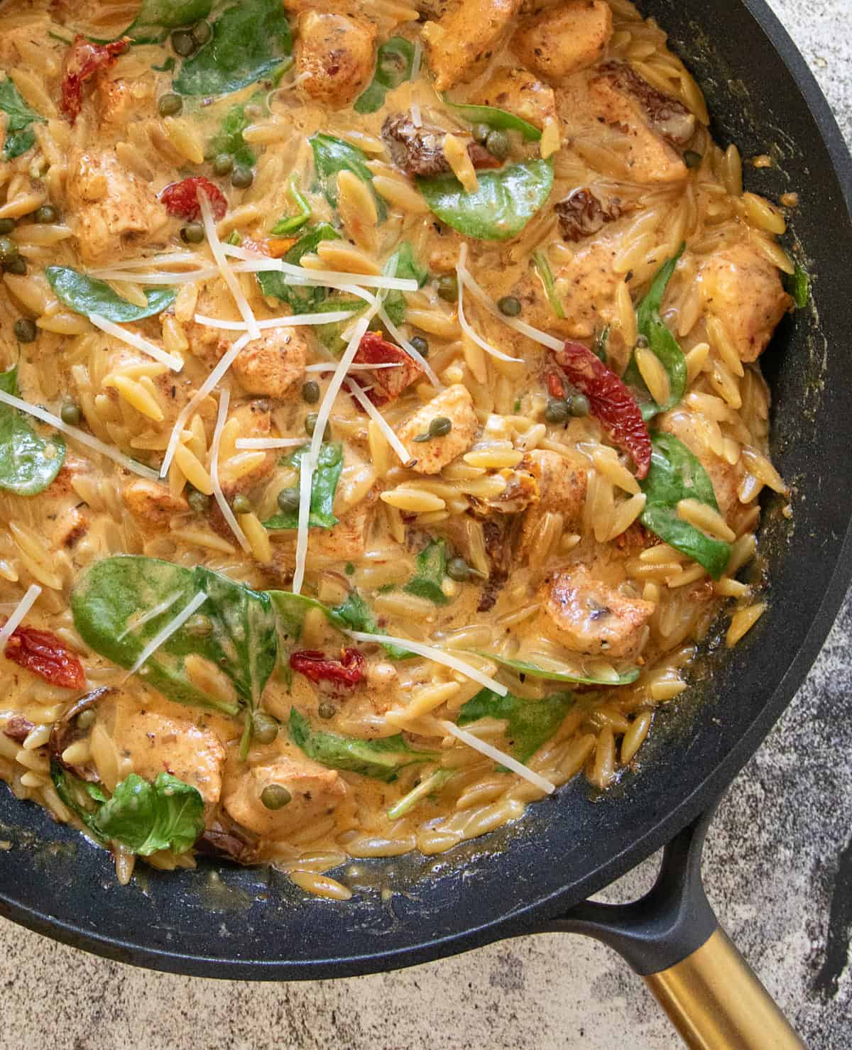 Closeup of One Pot Creamy Chicken Orzo with spinach, sun dried tomatoes, capers.