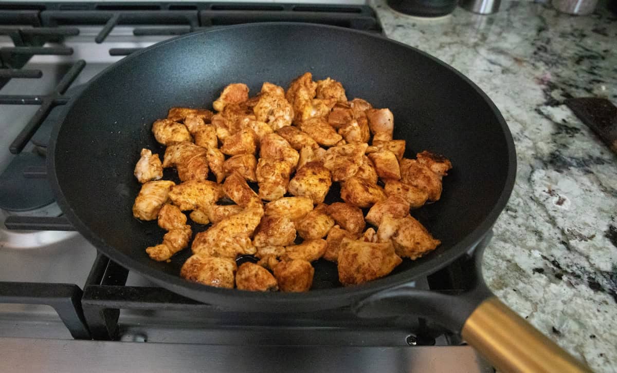 Seasoned chicken cooking in skillet.