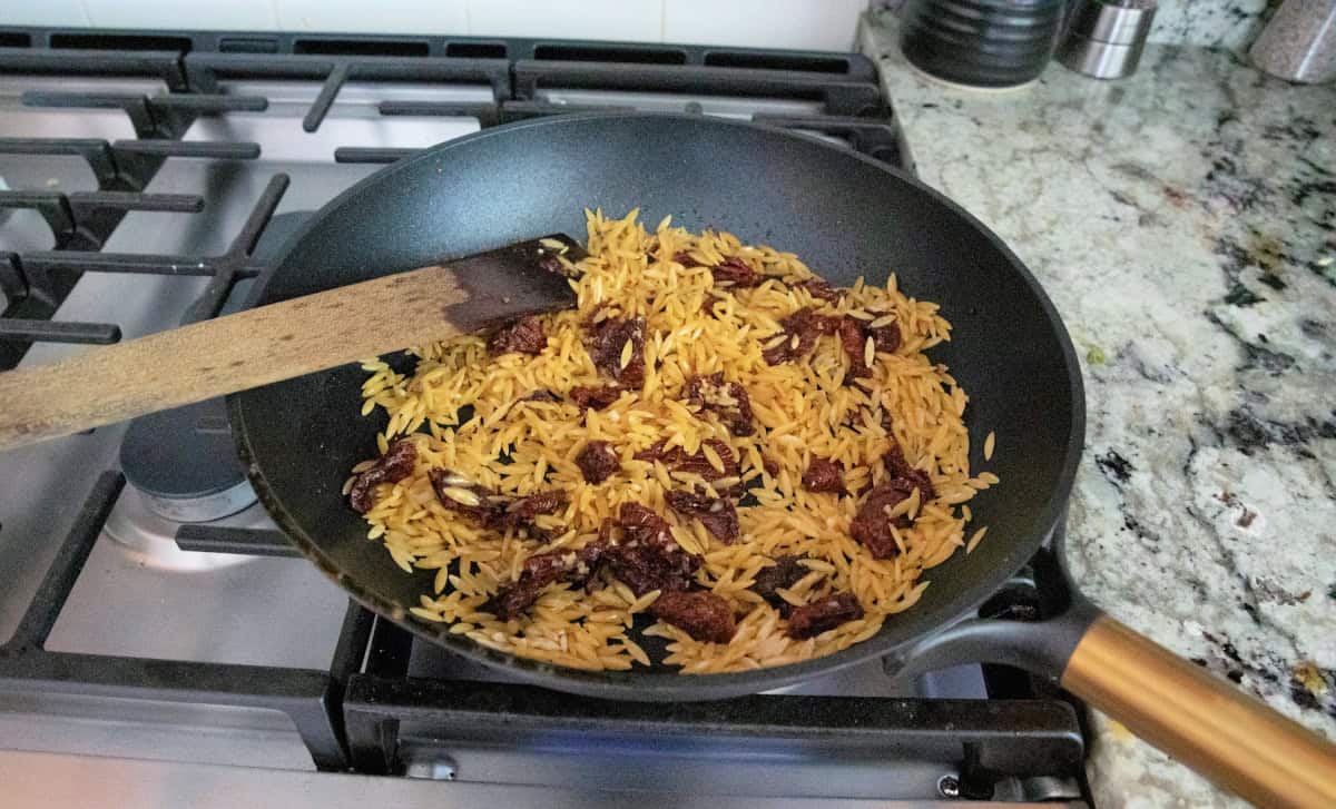Orzo, garlic, and sun dried tomatoes toasting in pan.