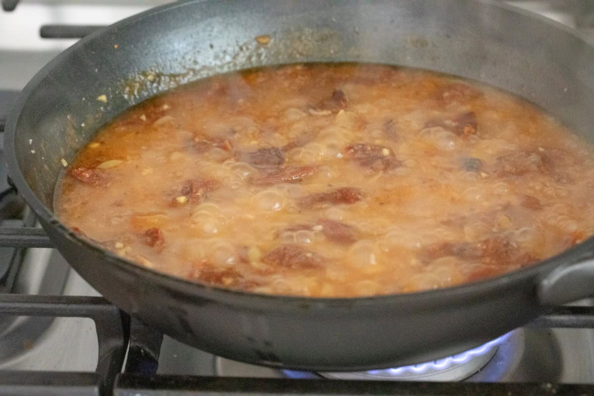Orzo and sun dried tomatoes cooking in chicken broth.