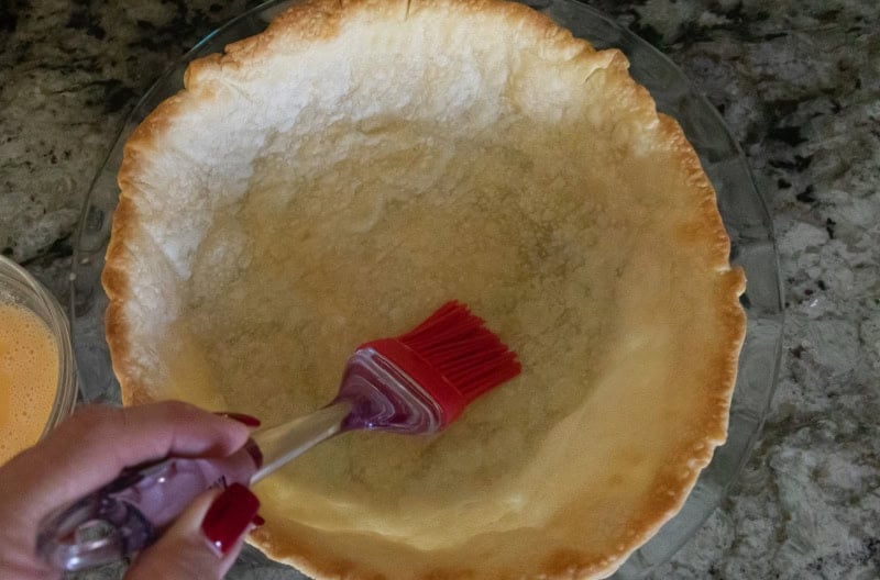 Par-baked pie crust with egg wash being brushed on.