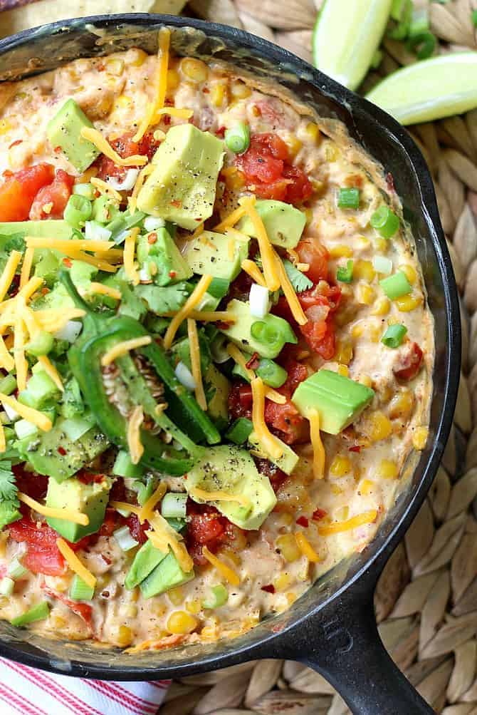 hot corn dip with fresh avocados jalapeno cheese onions and tomatoes on top in cast iron skillet