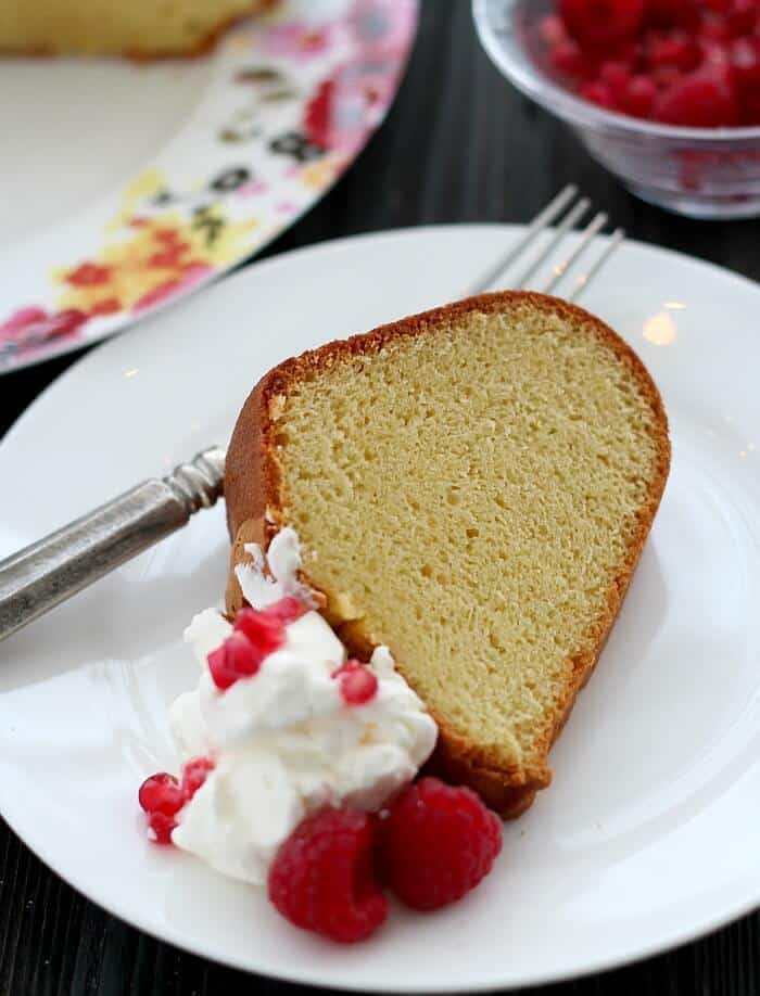 One slice of Perfect Pound Cake served with whipped cream and raspberries on a white plate