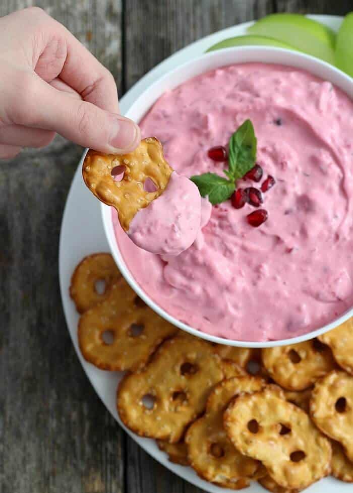 Cranberry Basil Dip on white plate with flat pretzel chips and one already dipped being lifted by my son
