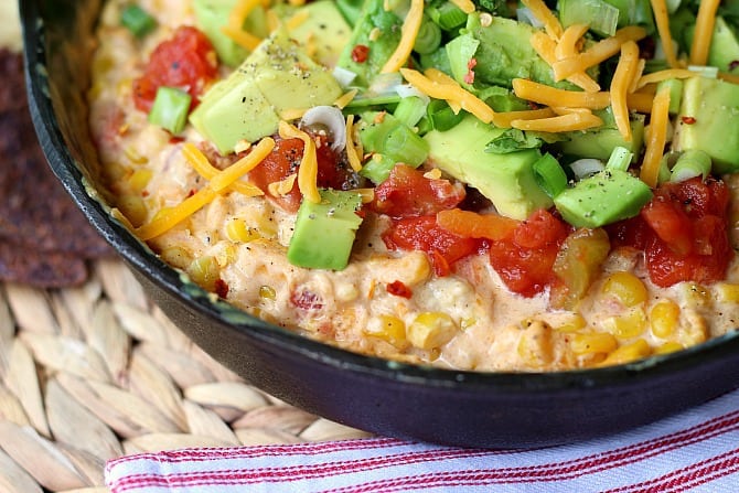 Hot Corn Dip topped with lettuce, avocado, cheese, tomatoes in a skillet