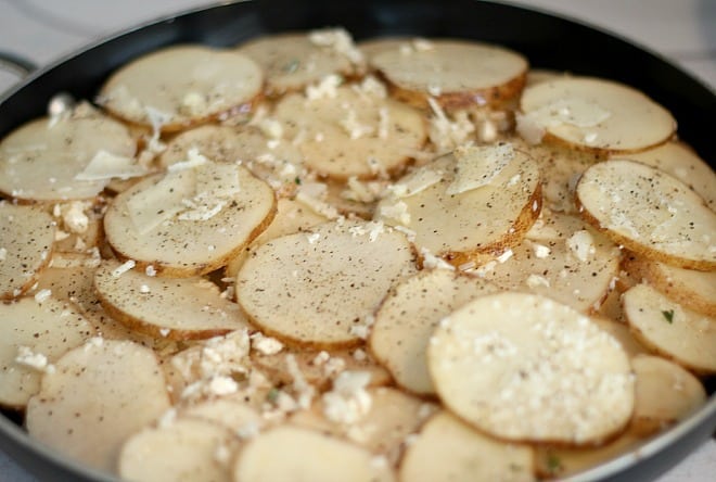Potatoes and onions and cheese layered in pan getting ready to bake