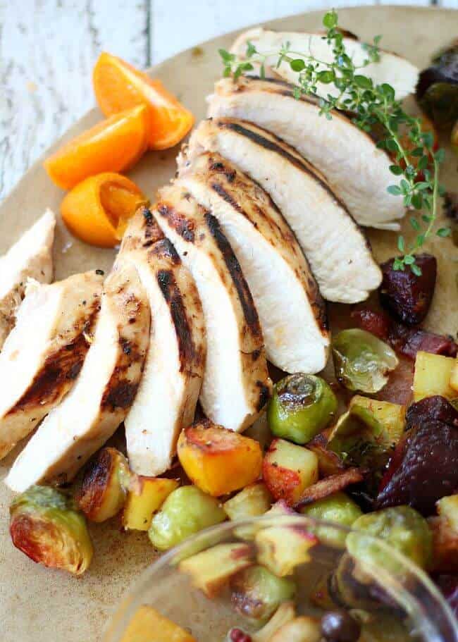 Sliced Citrus Marinated Chicken Breasts on serving platter with root vegetables. Orange slices