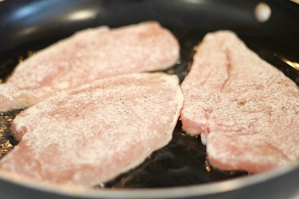 Chicken breast sprinkled with flour, cooking in a black pan