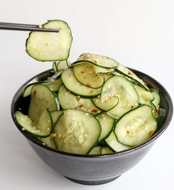 Cucumber Sesame Salad in black bowl. One slice held with chopsticks
