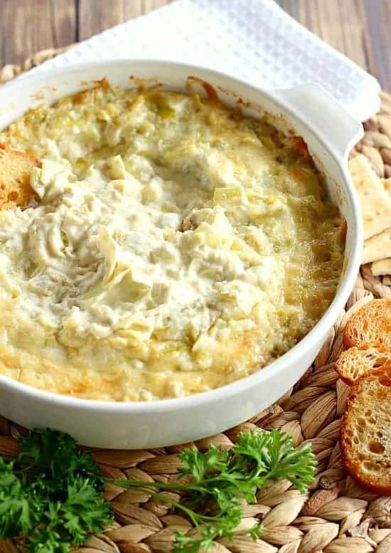 artichoke dip served in a white baking dish with parsley and bread on the side
