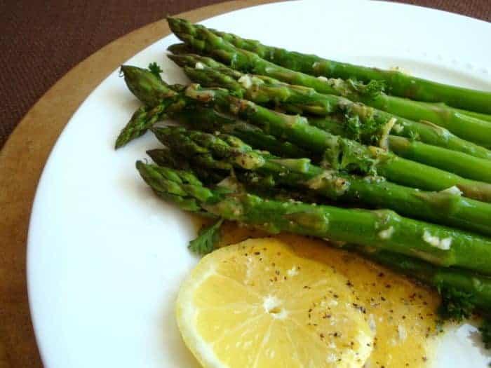 Roasted Asparagus and Dijion Lemon Sauce on a white plate with a slice of lemon on the side