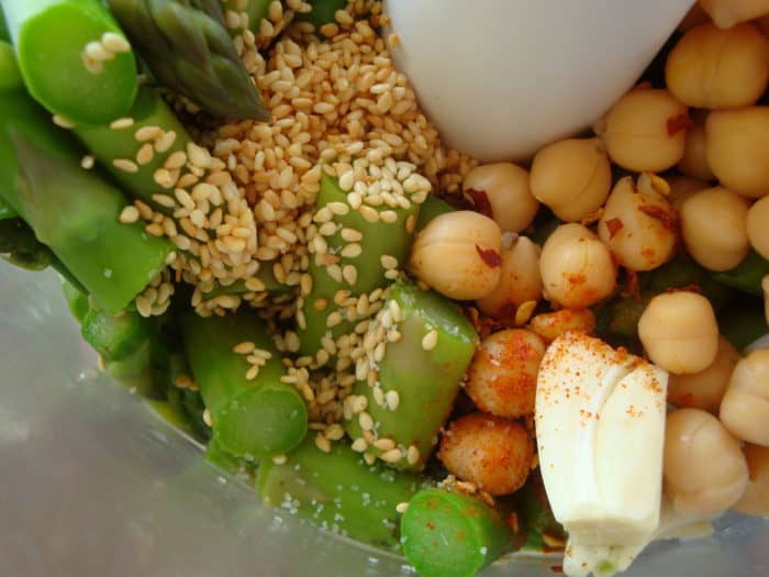Close up of chickpeas, sesame seeds, garlic, asparagus in processor 