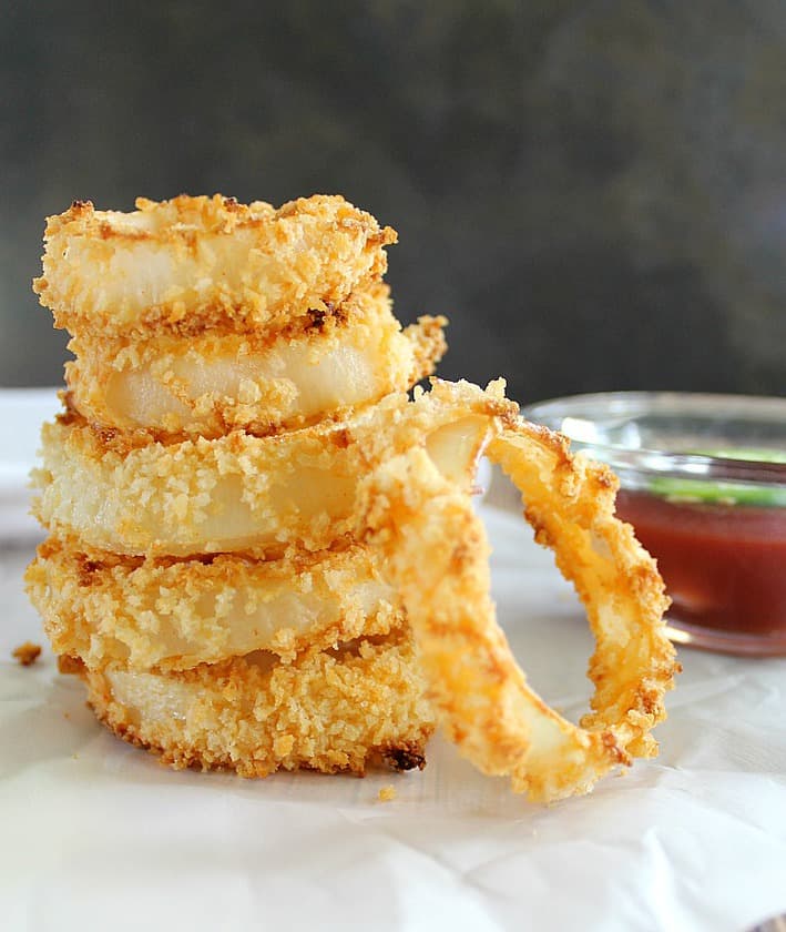 baked onion rings on parchment next to a bowl of ketchup with jalapeno on top
