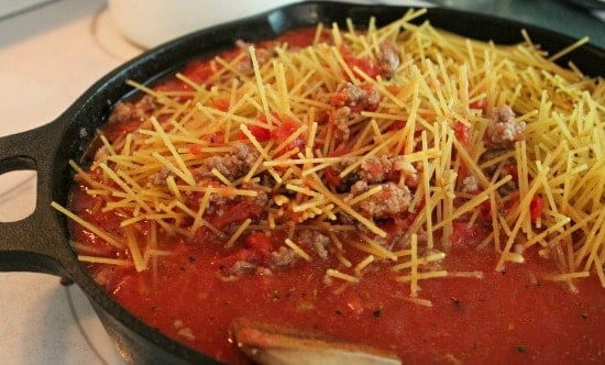 Uncooked spaghetti noodles, sauce and ground beef in a skillet to simmer
