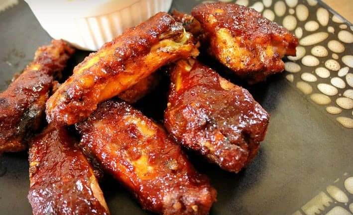 Barbecue Chicken Wings on a black plate with dip on the side 