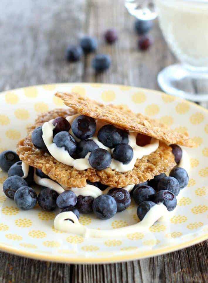 Oatmeal cookie crisps with blueberries and creme fraiche on a yellow and white plate