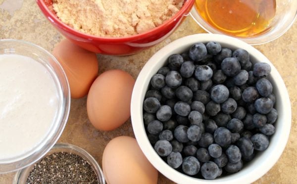 Coconut flour in red bowl, blueberries in white bowl, eggs, chia seeds, sugar, oil on the side