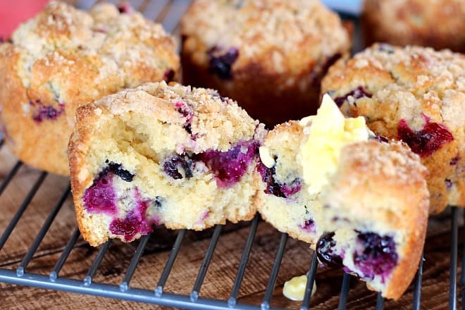  Blueberry Muffins on a cooling rack with one cut in half