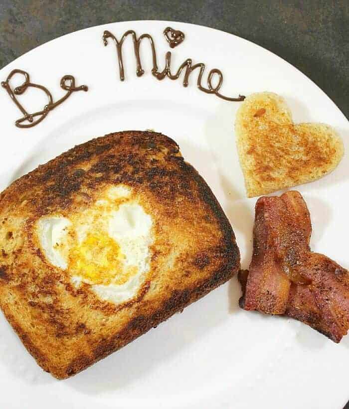 Breakfast for my Valentine with a heart-shaped bacon and toast and be mine written in chocolate on a white plate