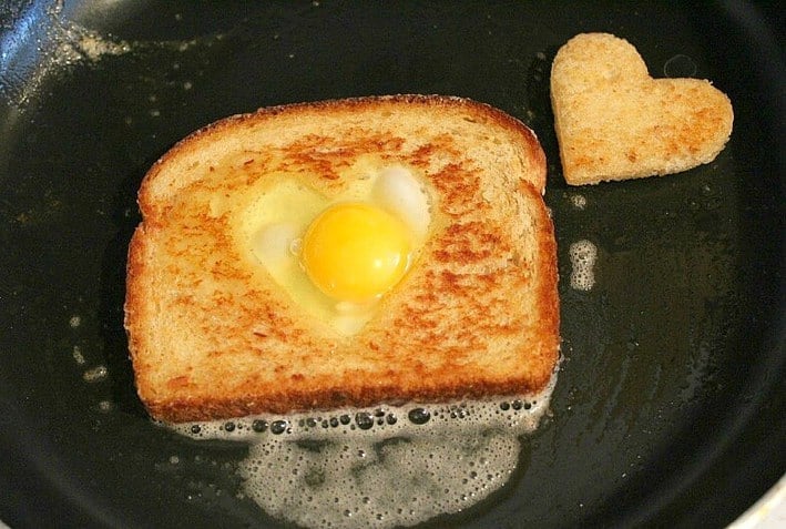 Toast cooking in a black pan with egg in the middle heart toast on the side