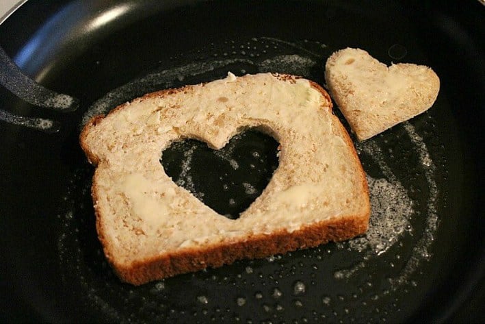 Buttered bread with heart cut out toasting in a black pan 