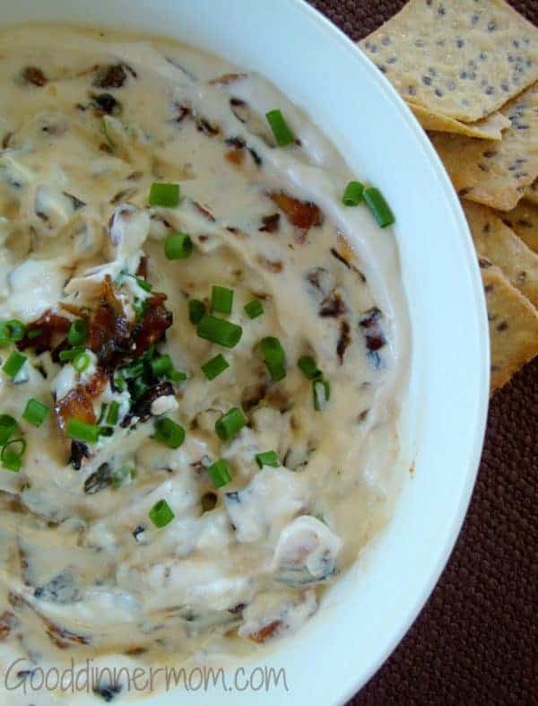 Caramelized French Onion Dip in white bowl with chives on top and crackers to side
