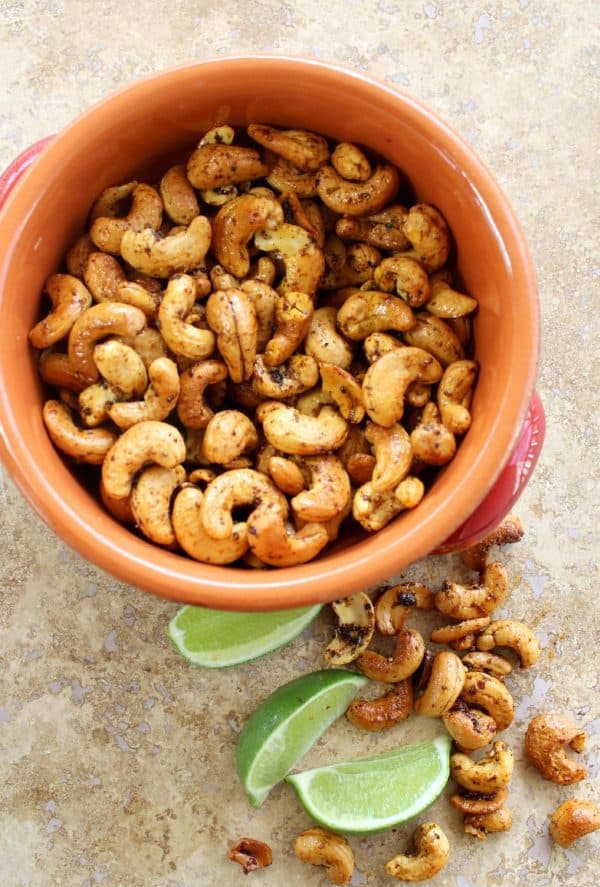 Seasoned cashews in an orange bowl with lime slices on the side