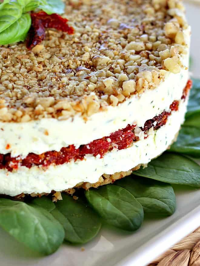 Cheese, Basil and Sun-Dried Tomato Torte side view on spinach on a white plate