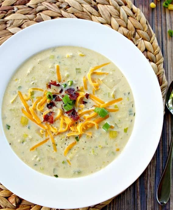 Corn Chowder with Summer Squash topped with shredded cheese and green onions served in a white bowl