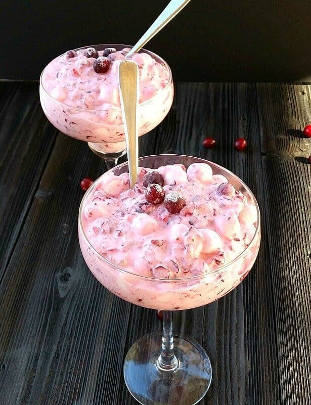 two glasses of cranberry salad with black background. Frozen cranberries on top, spoons in salad