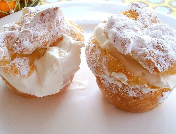Two Cream Puffs topped with powdered sugar, filled with whipped cram and custard on a white plate
