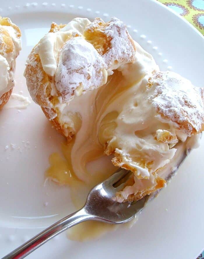 Cream Puffs on a white plate with a fork and one puff cut in half