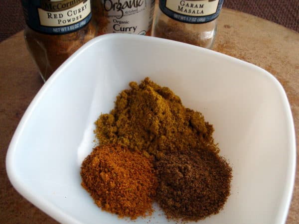 Curry powders and masala seasoning in a white bowl with seasoning jars in the back