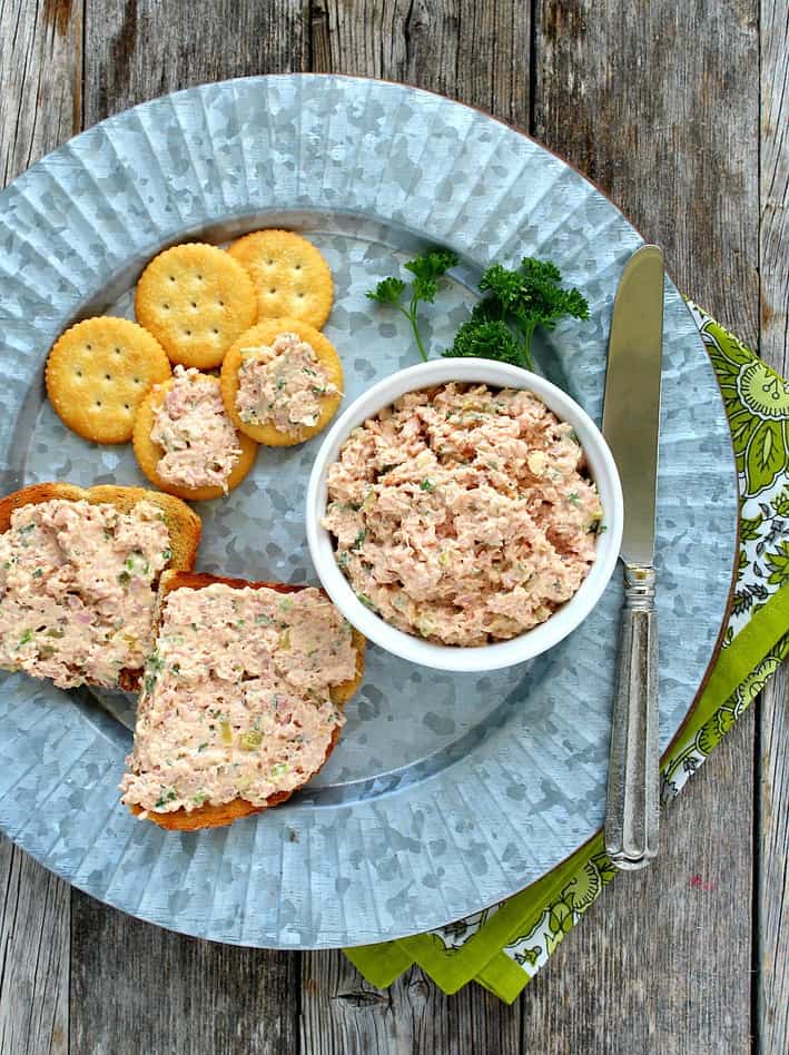 Deviled ham spread in a white bowl on a tin plate served on crackers and toast